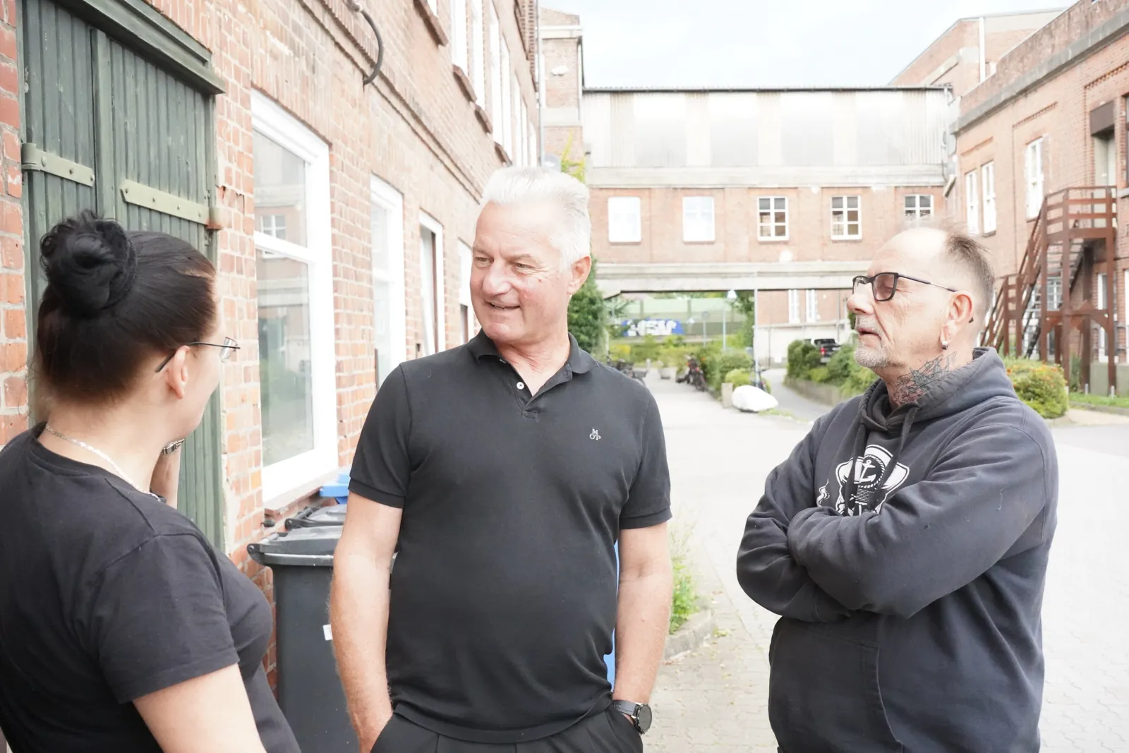 Frank Matthiesen im Gespräch mit zwei Menschen in einem Hof zwischen alten Backstein-Industriegebäuden.